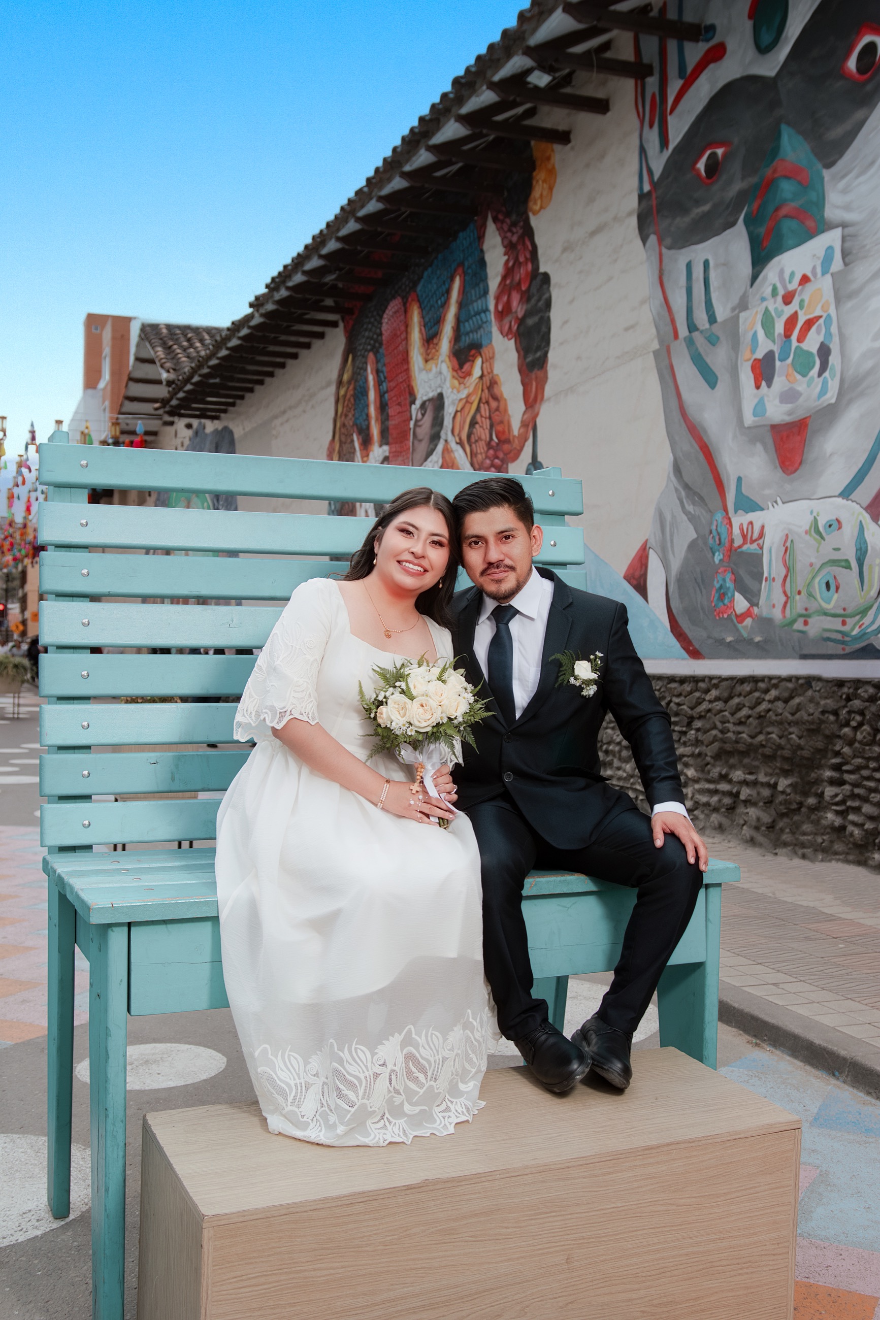 Recién casados sentados en una banca frente a un mural